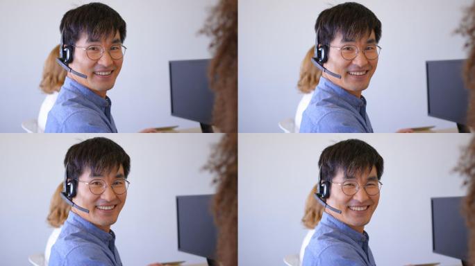 年轻的亚洲男性客户销售主管在现代办公室里用耳机4k说话