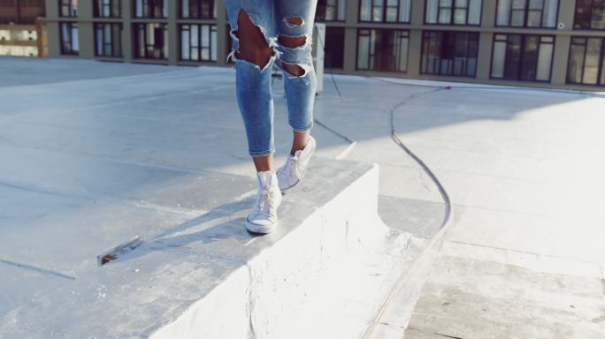 时尚年轻女子的双腿行走在城市的屋顶上
