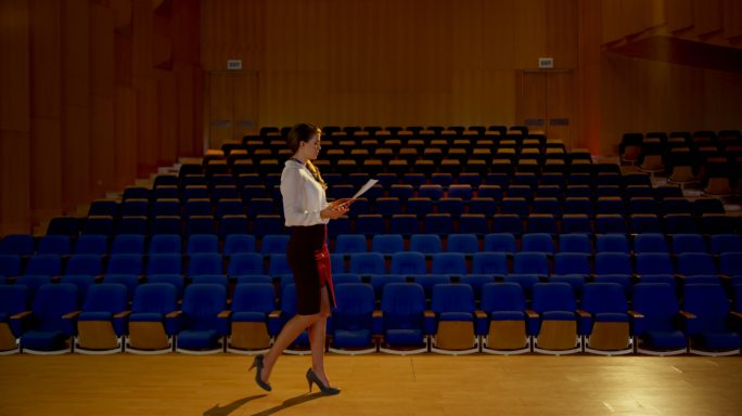 年轻的白人女商人在空旷的礼堂练习演讲