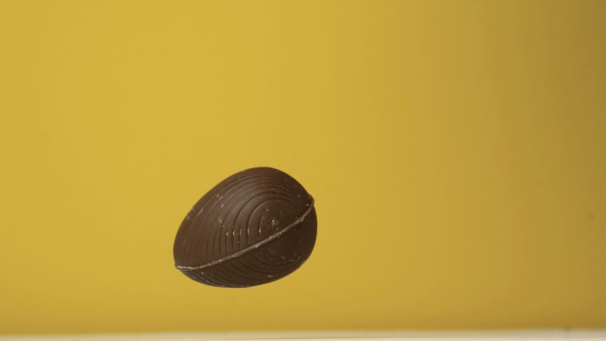 在慢镜头中，巧克力彩蛋在黄色背景下落下