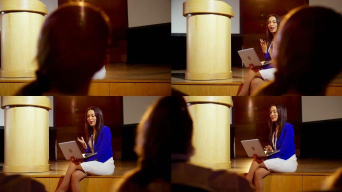 年轻的混血女商人拿着笔记本电脑在4k大礼堂的研讨会上发言