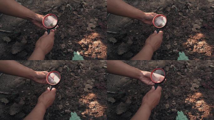 考古人员野外用放大镜观察研究埋在沙土文物