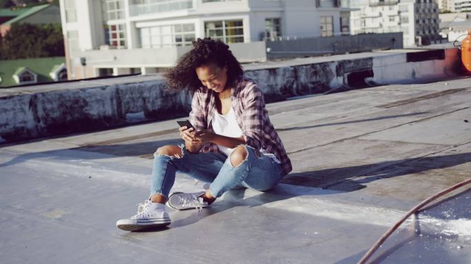 时尚的年轻女子在城市的屋顶上使用智能手机