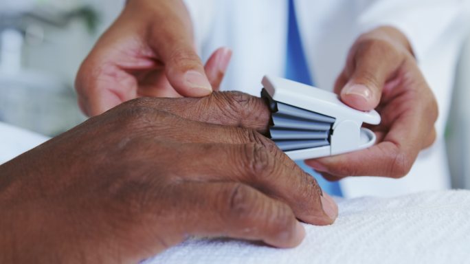 特写的非洲裔美国女医生附加脉搏血氧仪在男病人的手在病房