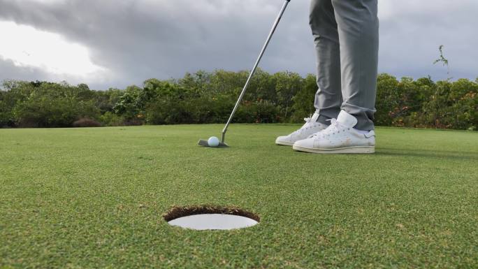高尔夫运动员在果岭上推杆入球洞的局部特写