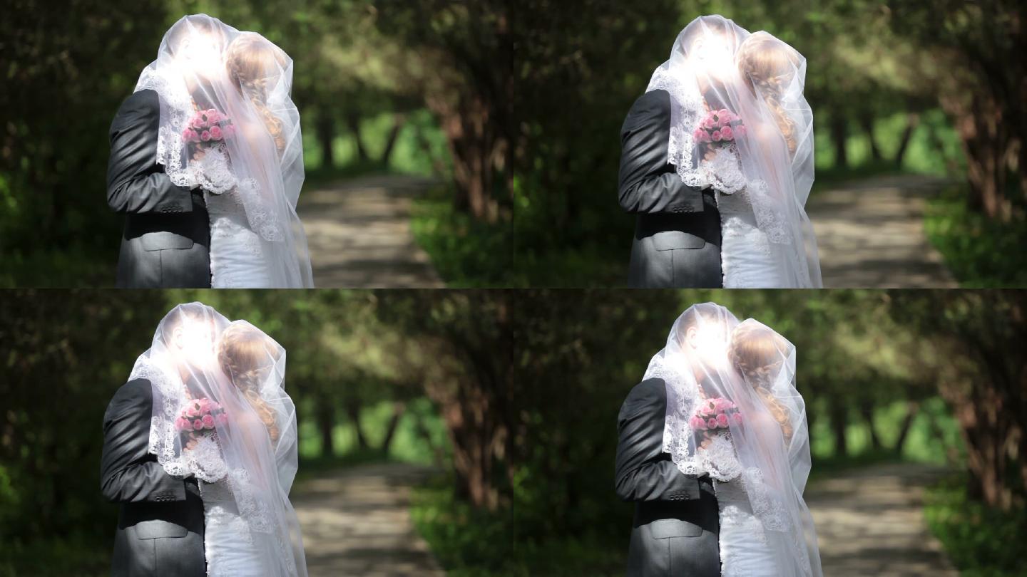 新郎在公园小巷亲吻戴着面纱的新娘