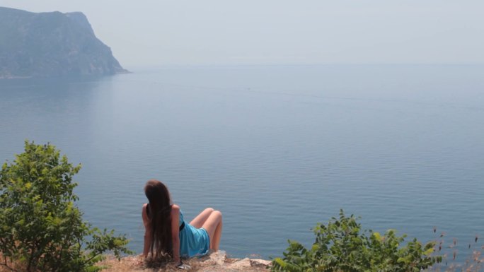 乌克兰克里米亚巴拉克拉瓦，一名年轻女子坐在黑海悬崖边上看海