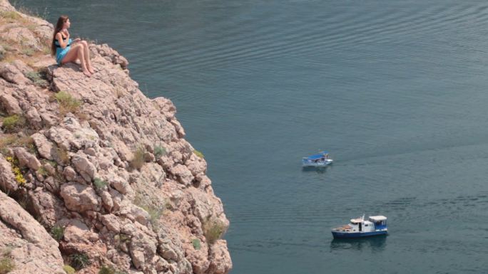 克里米亚巴拉克拉瓦湾黑海附近悬崖上休息的年轻女子