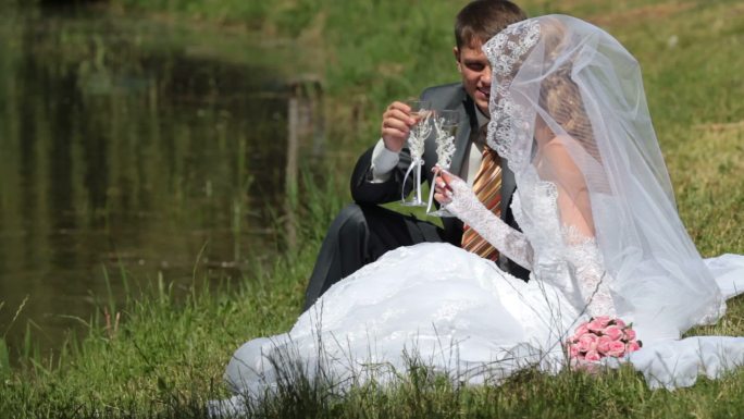 新娘和新郎坐在湖边喝香槟