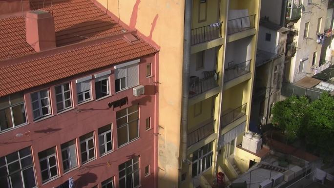 庭院和后院；相邻高层公寓楼；一个是粉红色的，屋顶是红砖；一个黄色带阳台。太阳照在房子上。