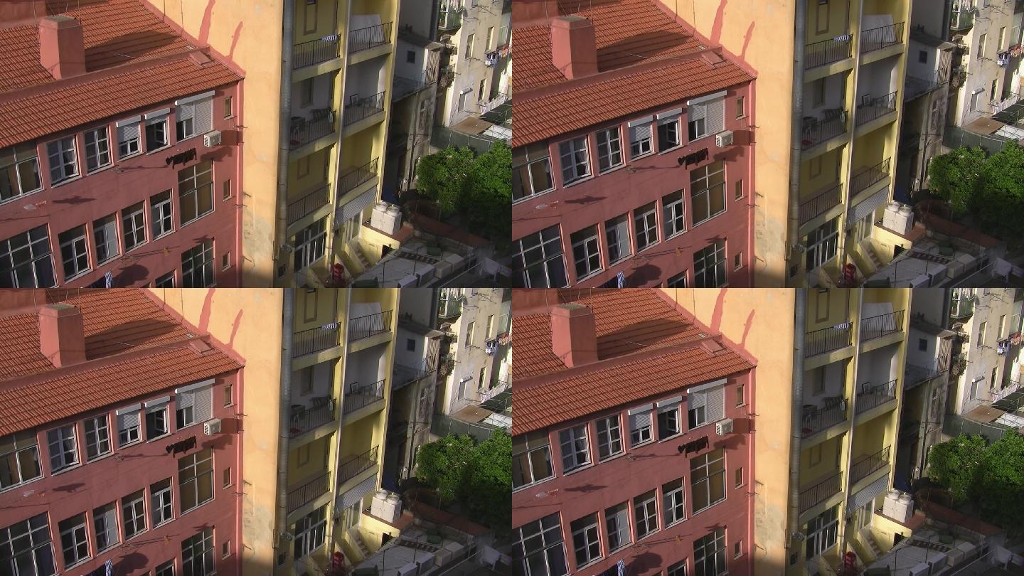 庭院和后院；相邻高层公寓楼；一个是粉红色的，屋顶是红砖；一个黄色带阳台。太阳照在房子上。