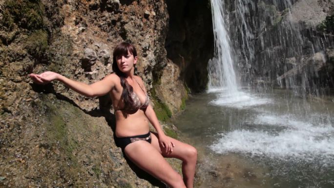 穿着比基尼的年轻女子在瀑布附近洗脸