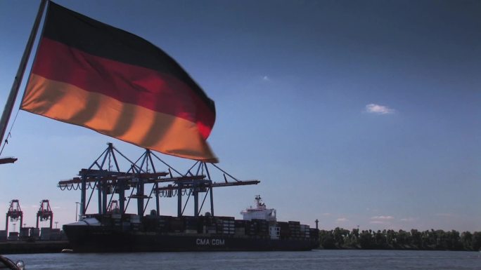 德国国旗挂在蓝天前，背景是Krsne和集装箱船。