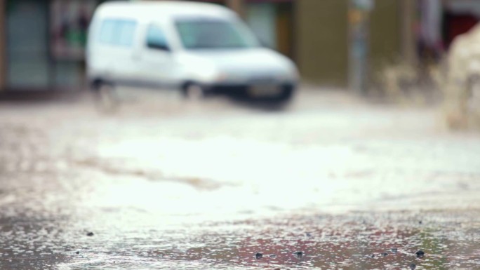 轿车在洪水泛滥的街道上翻过一个大水坑，溅起了水花