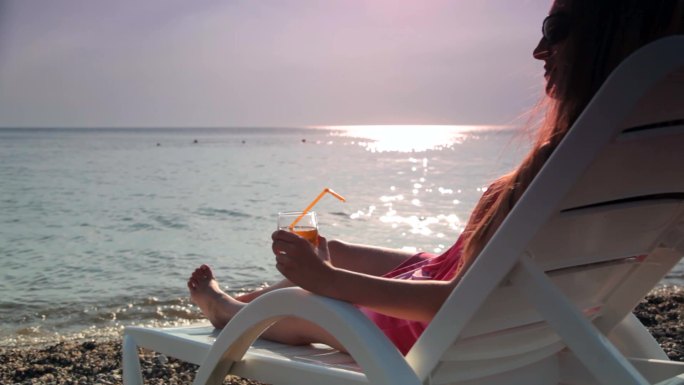 坐在海滩上喝鸡尾酒的女人看着日落
