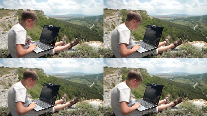 一个男孩在山上的悬崖边上操作他的笔记本电脑