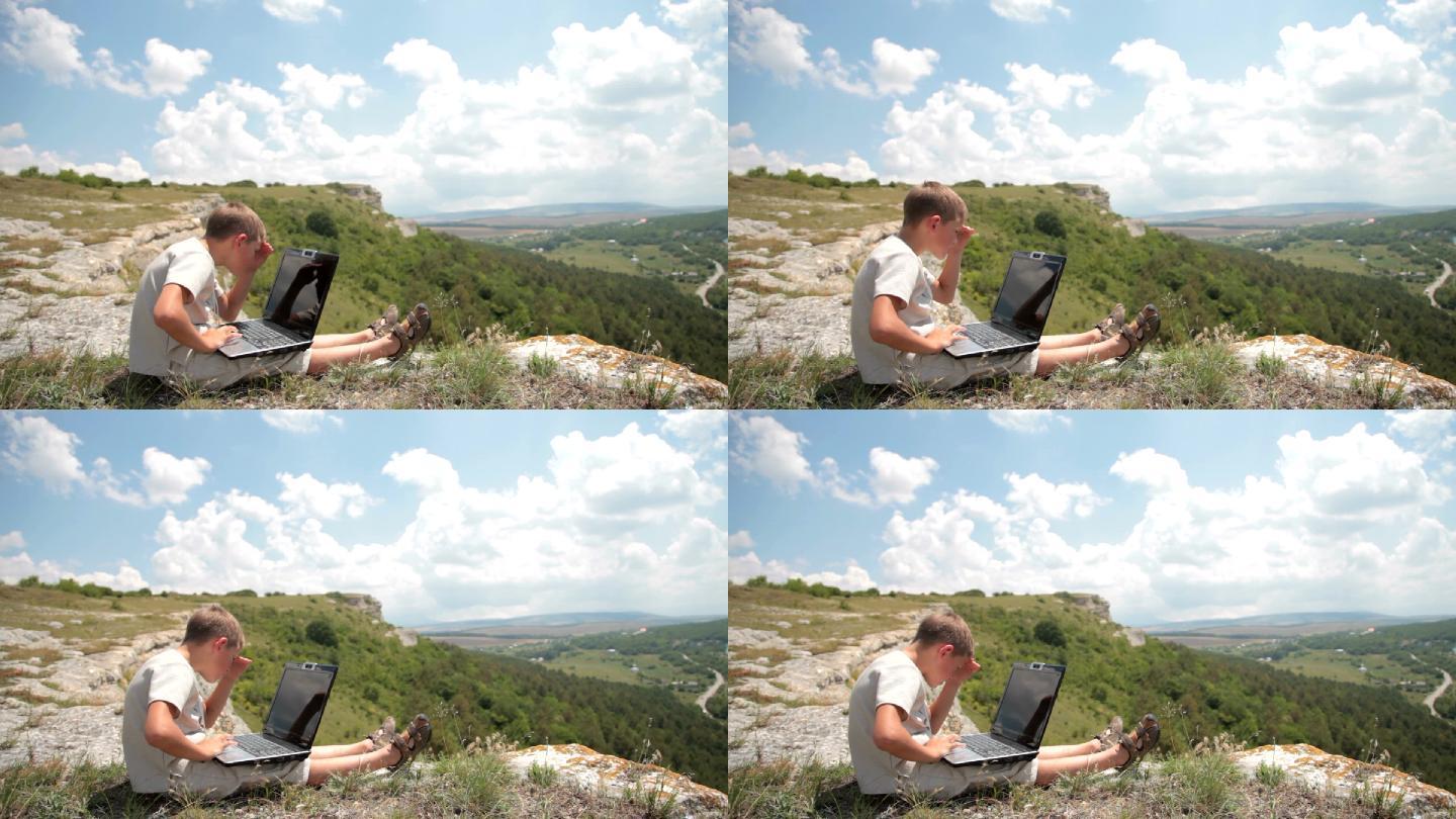 一个男孩在山上的悬崖边上操作他的笔记本电脑