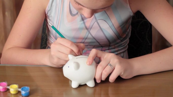 女孩计划在猪硬币盒上涂上颜色。