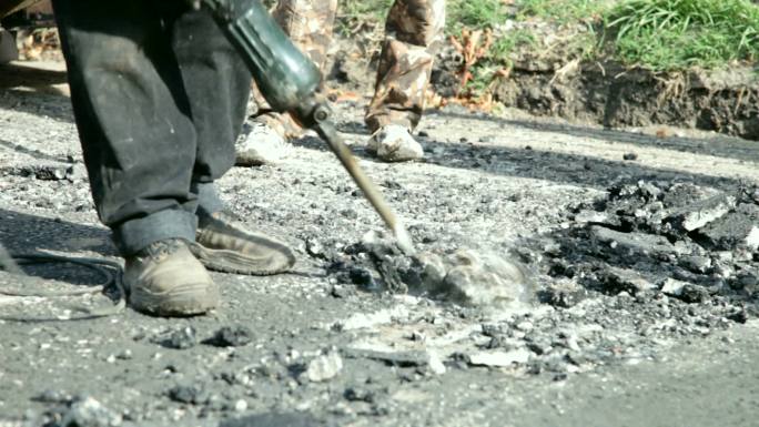 一名建筑工人用手提钻打碎道路上的沥青