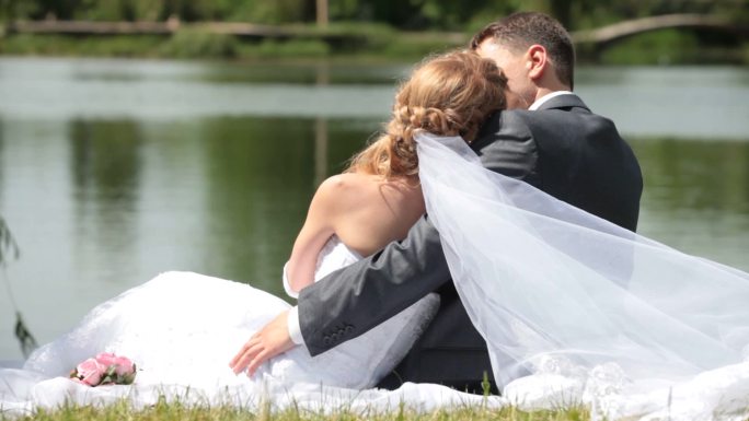 新婚夫妇坐在湖边互相拥抱