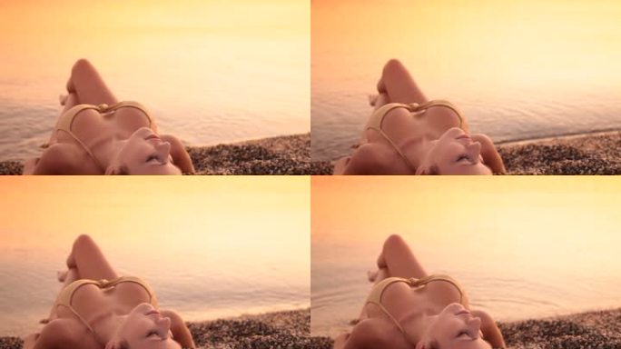 日落时，一位身穿比基尼的年轻女子躺在海边的海滩上