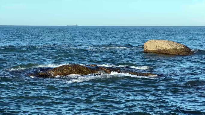 深蓝色海平面海浪和礁石远处轮船