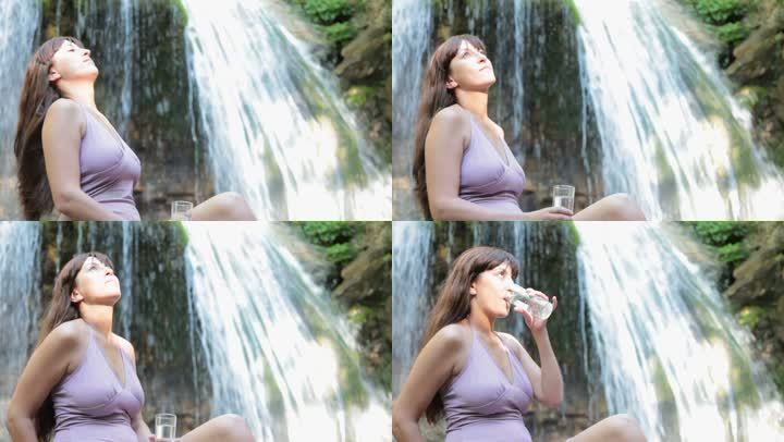 从瀑布边的塑料瓶里喝水的漂亮女人
