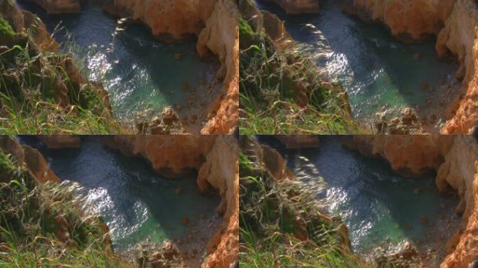 从一块高高陡峭的长满草的岩石到一个被裸露的悬崖环绕的岩石海湾；太阳在浅绿色的水中闪闪发光；葡萄牙阿尔