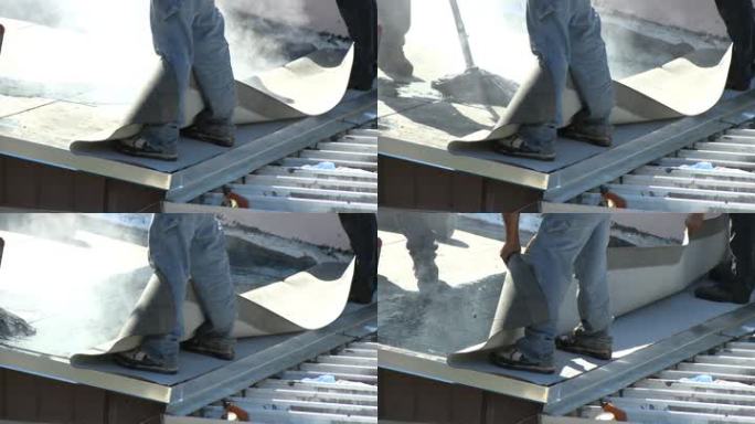 屋顶工人在平屋顶上使用热沥青安装最后一层膜。