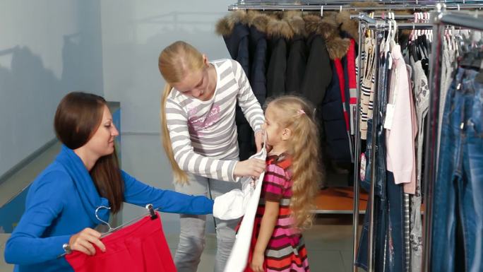 母亲带着两个女儿在一家服装店买女孩的衣服，看起来像裙子和毛衣