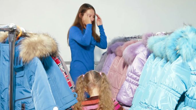 母亲和女儿在服装店买冬衣，孩子在试羽绒服