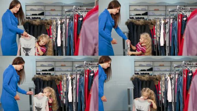 母亲和女儿在服装店买女孩的衣服，有趣的小女孩正在试穿束腰毛衣