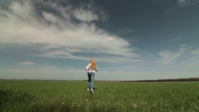 快乐的金发小女孩在春天的田野上奔跑