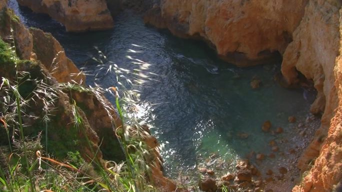 从高陡的岩石到被裸露的悬崖环绕的岩石海湾；浅绿色水域；葡萄牙阿尔加维海岸。