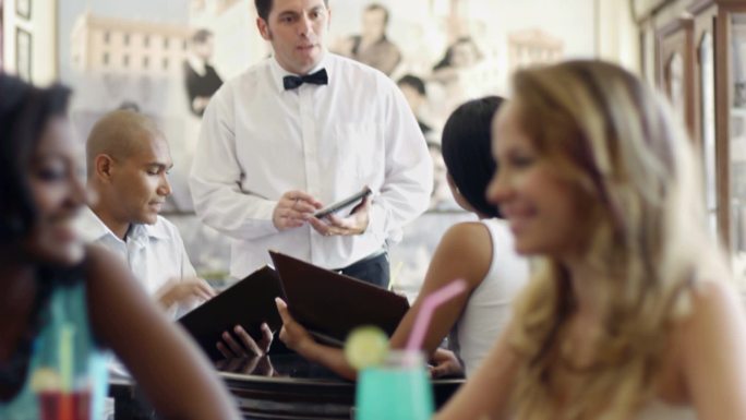 一对年轻的西班牙裔夫妇在餐厅用餐，并打着领结和服务员交谈。
