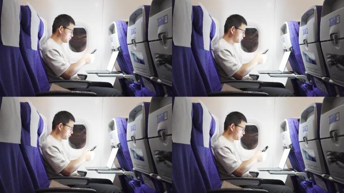 男子在飞机上使用笔记本电脑和手机