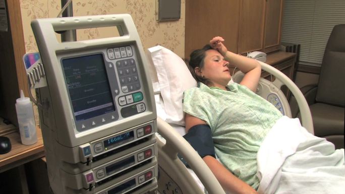 一名妇女躺在医院病床上，旁边是监控设备