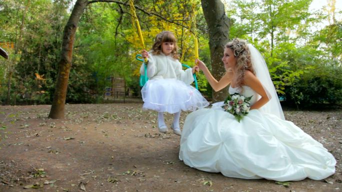 在秋天公园的秋千上，新娘和一个打扮成新娘的小女孩在一起