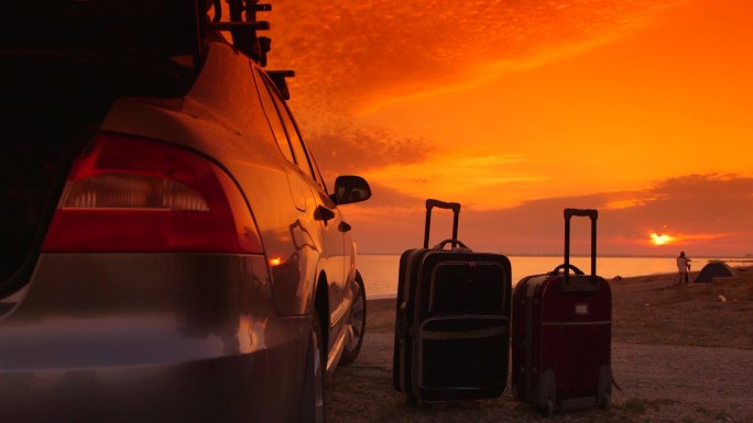 夏日海滩度假目的地两个行李箱在车旁夕阳下的年轻夫妇在后台