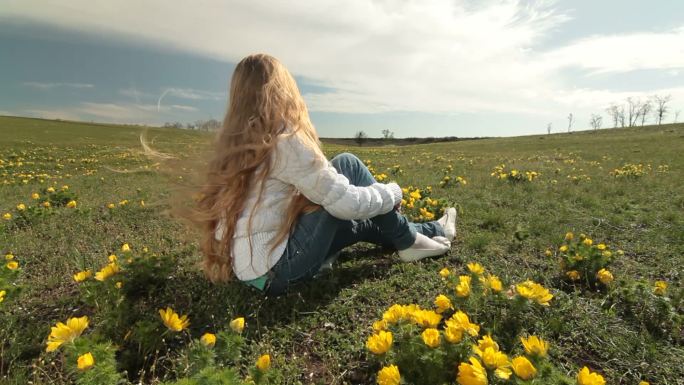 金发碧眼的小女孩坐在春天的野黄色牡丹草地上