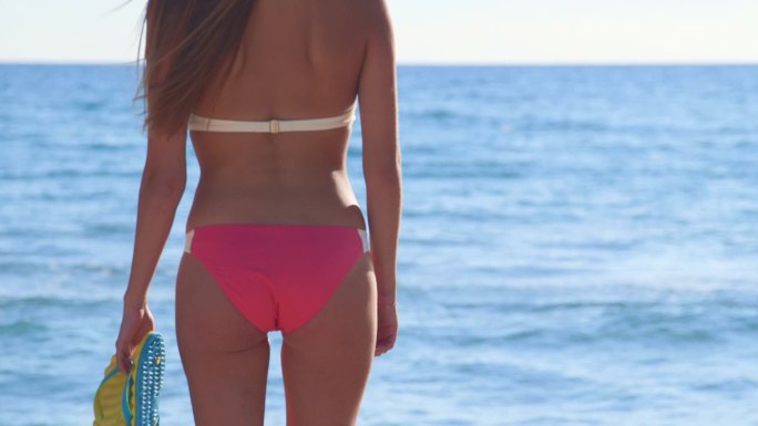 夏日海滩上穿着粉色比基尼和人字拖的女孩