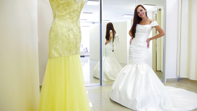 年轻迷人的新娘在婚纱店试穿婚纱，摆出姿势看着摄像机