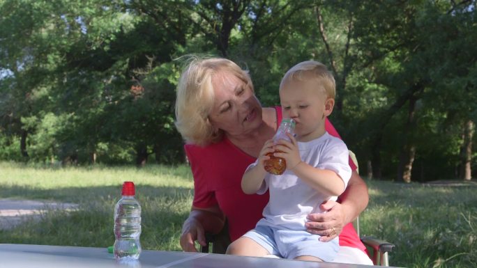 奶奶和孙子在公园里，孩子在喝果汁