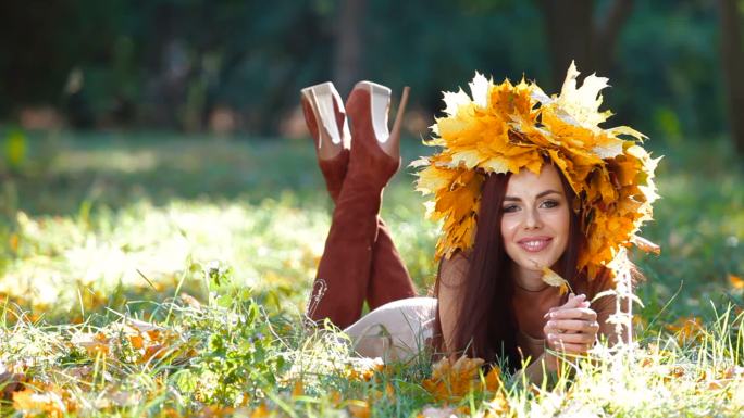 年轻迷人的女人在秋天公园里摆好姿势，看着摄像机，微笑着