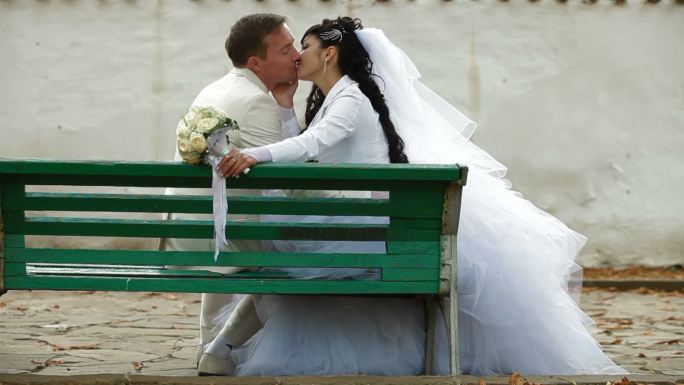刚刚结婚的夫妇坐在秋天公园的侧视图