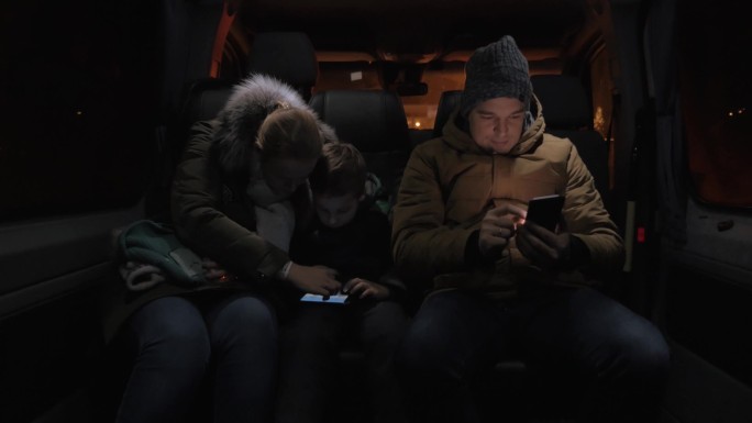 三名乘客在深夜乘坐小型公共汽车。母亲和儿子用智能手机娱乐，男人用手机浏览打发时间