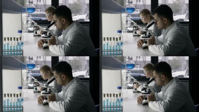 两位年轻的研究科学家在现代实验室通过显微镜研究新物质或病毒。年轻英俊的混血科学家在实验室进行实验，而