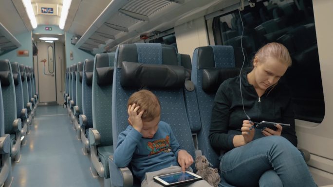 母亲和孩子乘坐夜间特快列车。当男孩玩数字平板电脑时，女人花时间在智能手机上充电