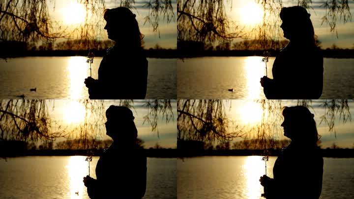 夕阳下清澈的湖边，美丽的女士带着花的剪影