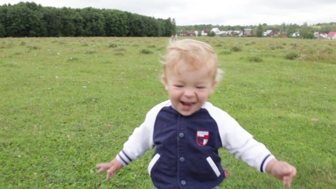 第一步。微笑和大笑。这个一岁的可爱的金发男孩正在迈出他第一个独立的步伐，并享受其中。使用凸轮稳定设备